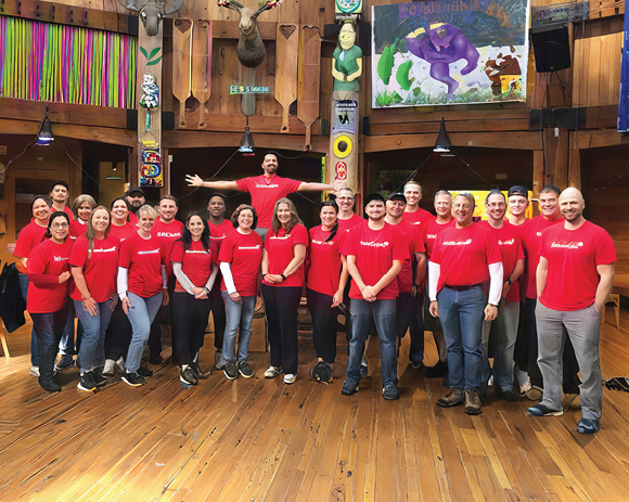 large group in Travelers T-shirts posing in a wooden lodge