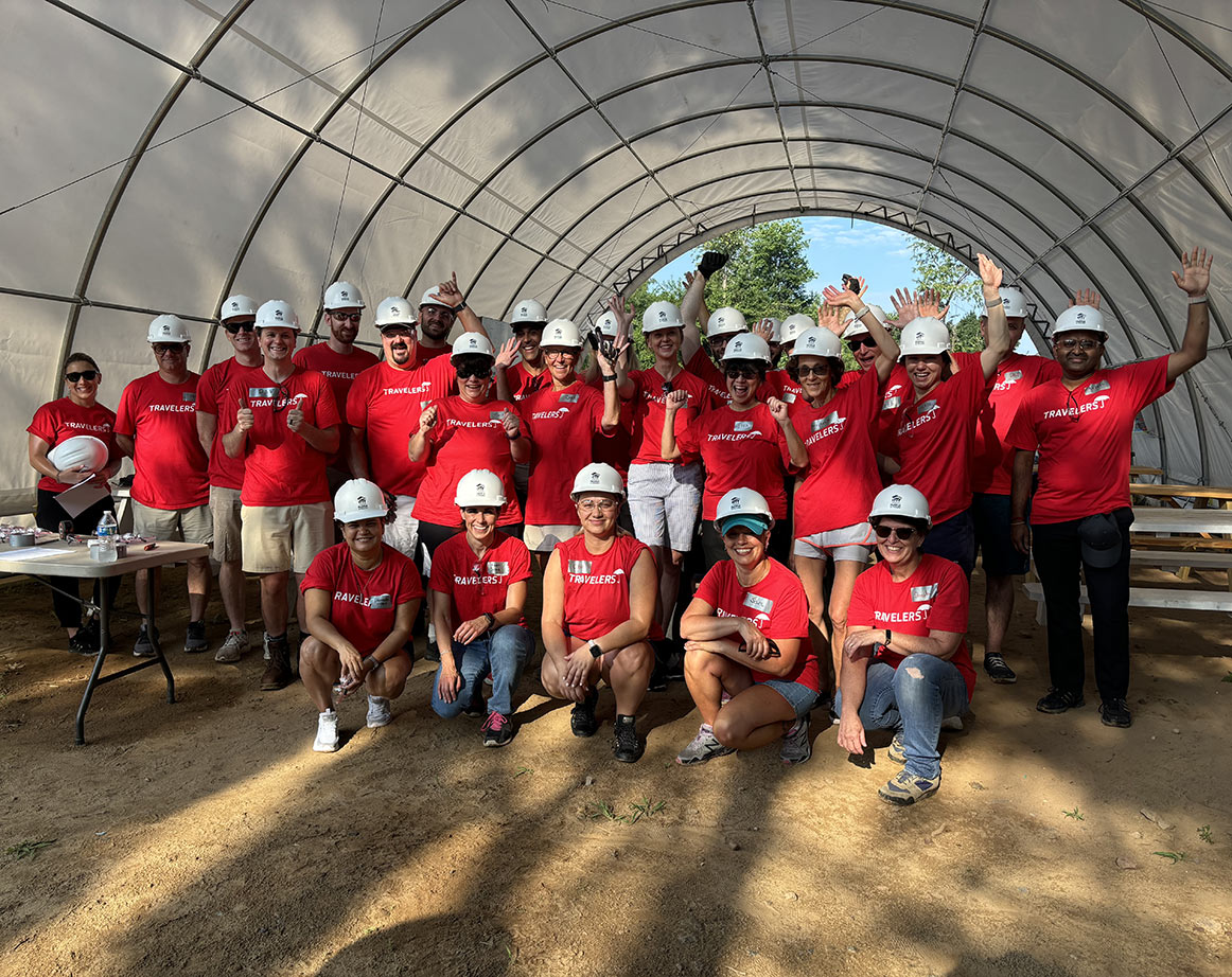 large group of employees in red T-shirts and hardhats under an arched tent