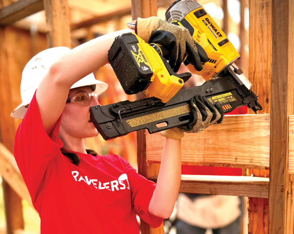 woman in a red T-shirt and hardhat using a large staple gun