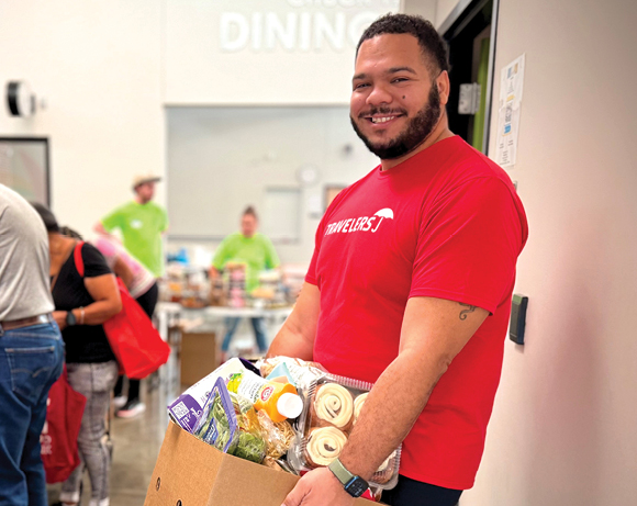 a man in a Travelers T-shirt carrying a box of groceries