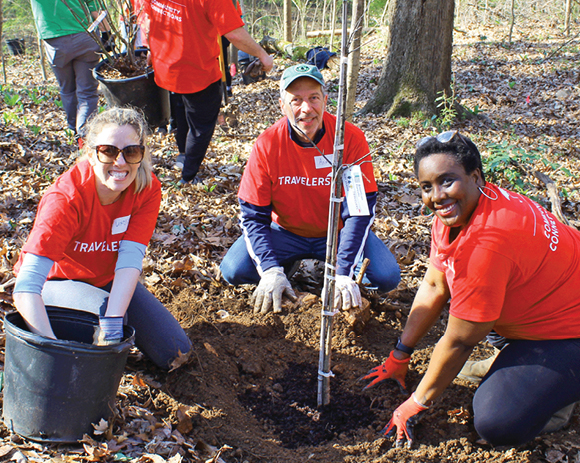 three people in Travelers T-shirts kneeling, planting a tree