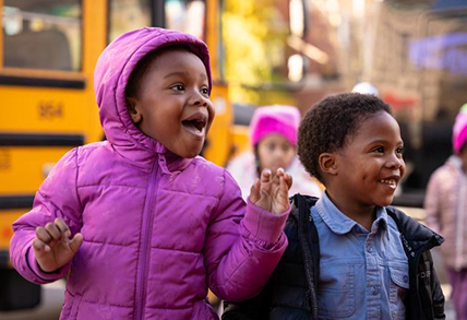 young happy children in front of a school bus